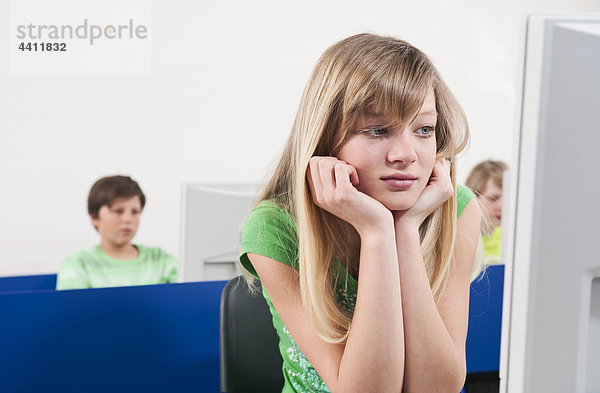 Teenager-Mädchen (14-15) mit Kopf in der Hand  Jungen mit Computer im Hintergrund