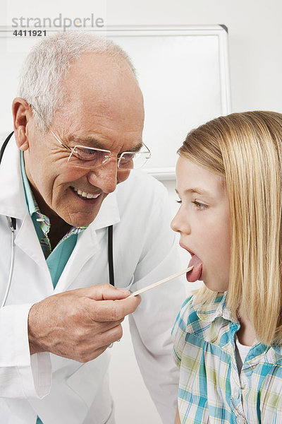 Arzt untersuchendes Mädchen (8-9) mit Zungenspatel