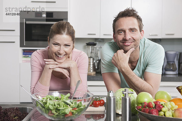 Deutschland  Paar mit Gemüse und Obst auf Küchenarbeitsplatte  lächelnd  Portrait