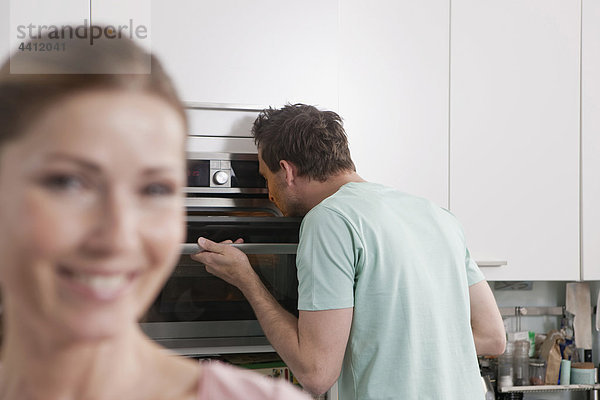 Deutschland  Mann schaut in den Ofen mit lächelnder Frau im Vordergrund
