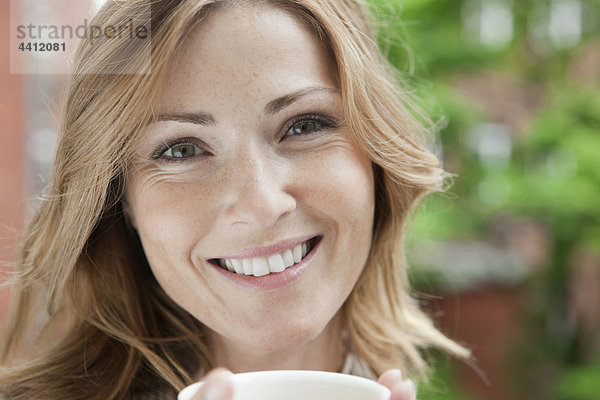 Deutschland  Frau hält Kaffeetasse  Porträt  lächelnd