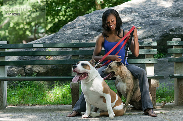 Frau sitzt auf einer Parkbank mit ihren beiden Hunden