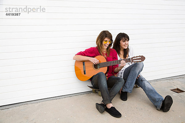 Zwei Mädchen auf dem Boden sitzend mit Gitarre