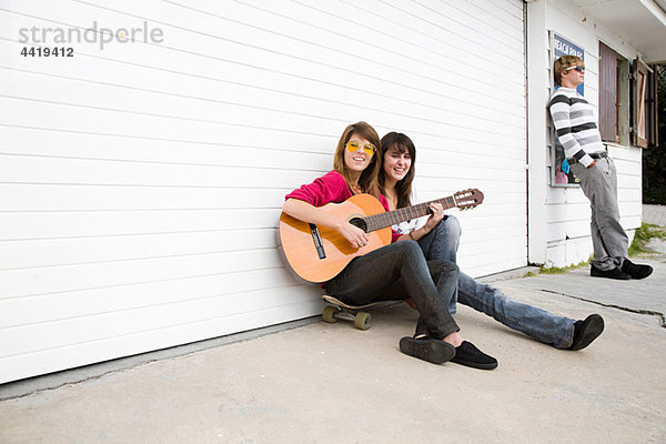 Zwei Mädchen sitzen auf Boden mit Gitarre