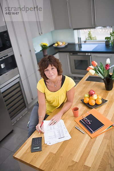 Frau sitzt in Küche mit Rechnungen  Portrait