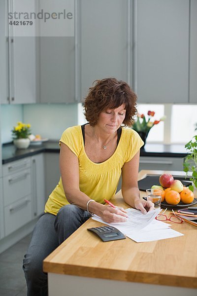 Frau sitzt in Küche mit Rechnungen
