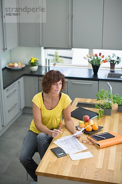 Frau sitzt in Küche mit Rechnungen