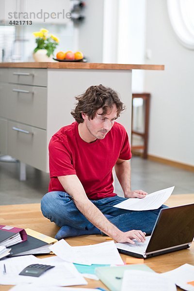 Mid-adult man working from home  using laptop on kitchen floor