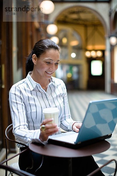 Reife geschäftsfrau arbeiten auf Laptop  halten Kaffee zum Mitnehmen