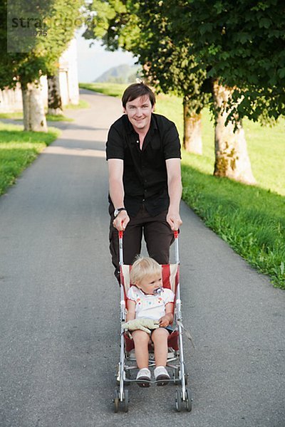 Vater Tochter in Kinderwagen im Park zu tragen
