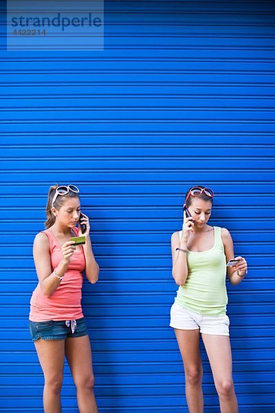 Zwei Girls vor der blauen Wand  sprechen auf Handys