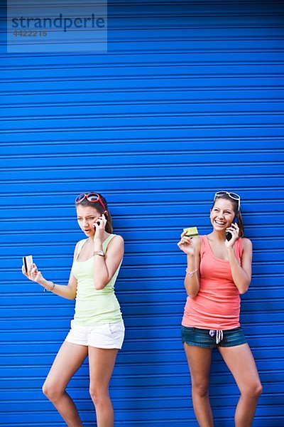 Zwei Girls vor der blauen Wand  sprechen auf Handys