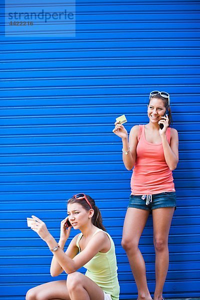 Zwei Girls vor der blauen Wand  sprechen auf Handys