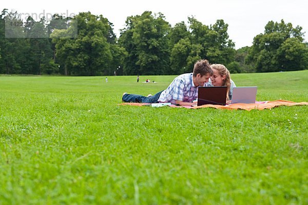 Mitte adult paar liegend auf Decke im Park mit laptops