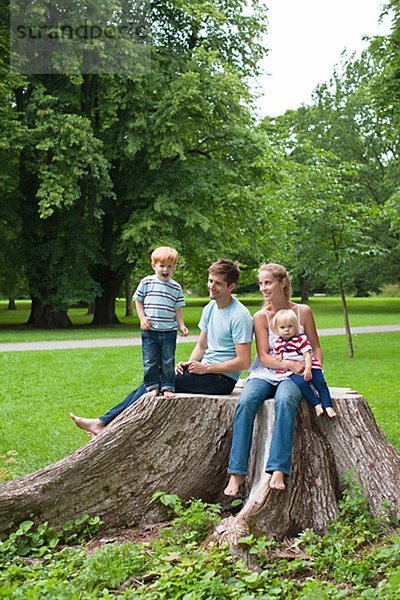 Mitte adult Paar mit Kindern sitzen auf Stub im Park und lächelnd