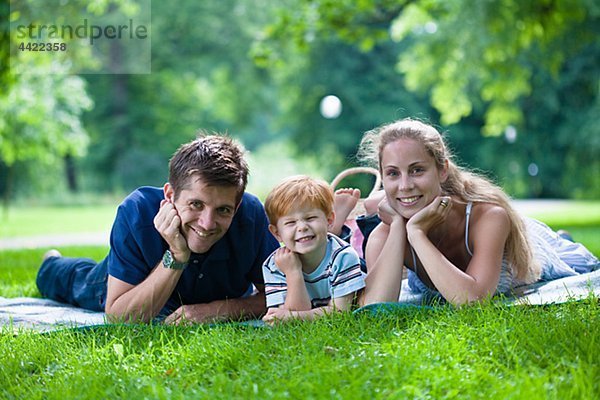 Eltern mit Sohn im Park liegen und Blick in die Kamera