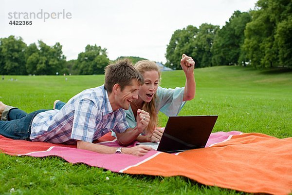 Glückliches Paar im Park liegen und benutze laptop