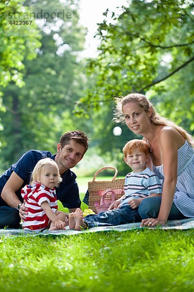 Eltern mit den Kindern im Park sitzt und Blick in die Kamera