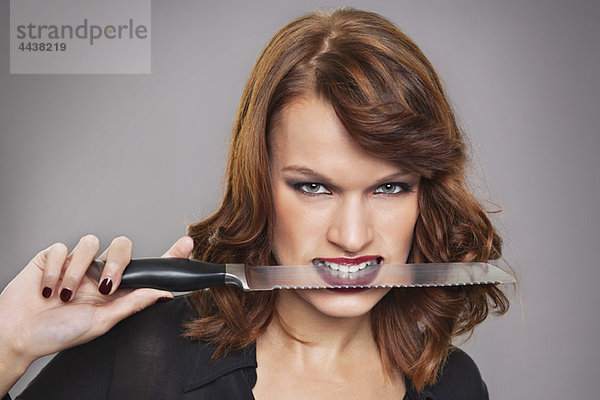 Junge Frau mit Messer zwischen den Zähnen