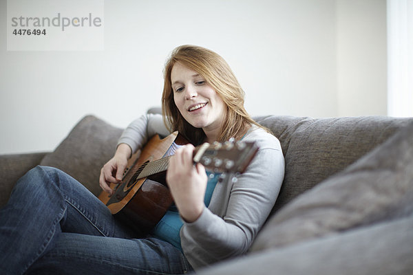 Mädchen sitzt auf dem Sofa und spielt Gitarre.