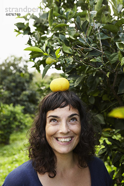Frau balanciert Mandarine auf dem Kopf