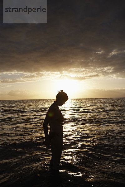 Frau steht im Meer bei Sonnenuntergang