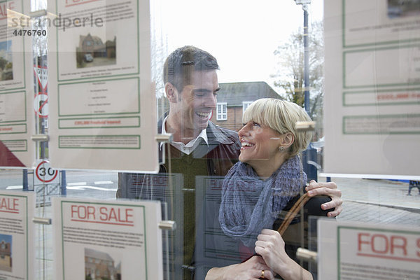 Paar  das in das Fenster des Immobilienmaklers schaut.