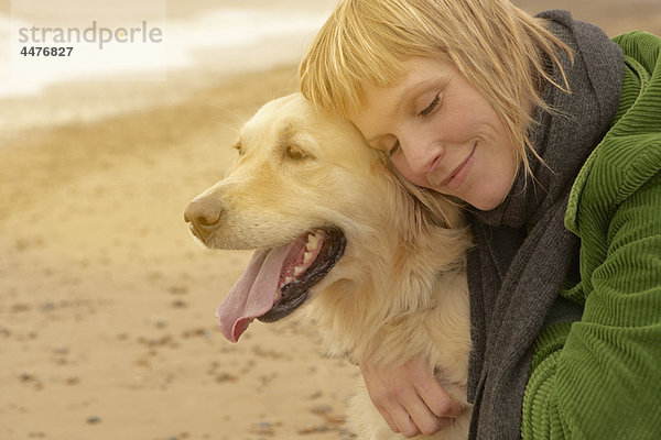 Frau umarmt Hund am Strand