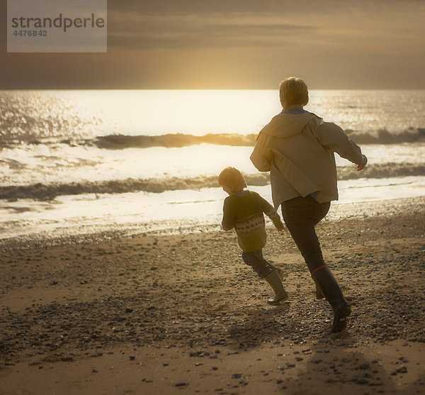 Eine Frau jagt einen kleinen Jungen am Strand. Herbst