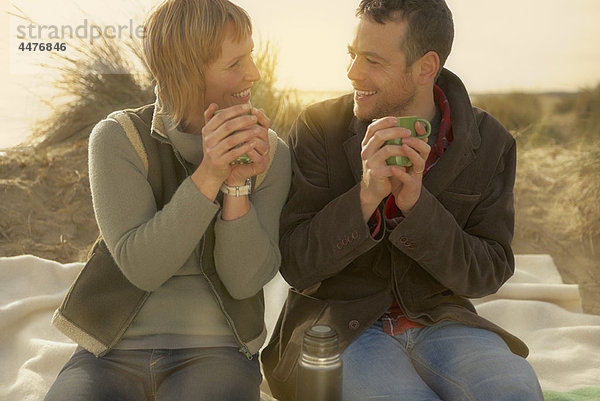 Paar am Strand bei Kaffee aus der Flasche