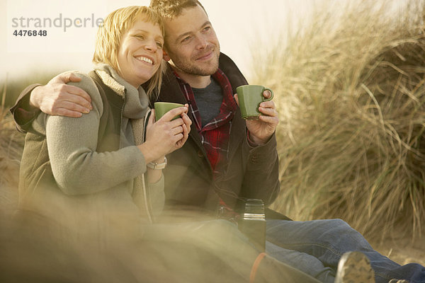 Paar am Strand bei Kaffee aus der Flasche