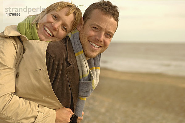 Frau umarmt Mann von hinten am Strand