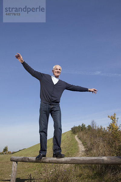 Älterer Mann beim Balancieren auf einem Holzklotz