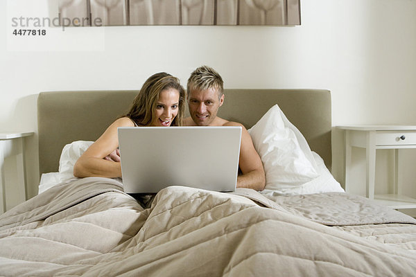 Junges Paar mit Laptop im Bett