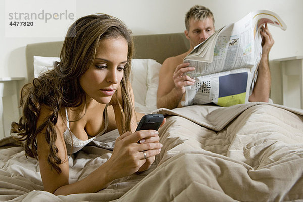 Junge Frau mit Smartphone im Bett