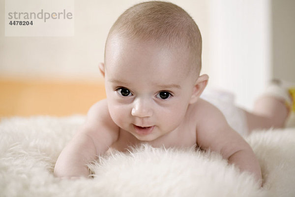 Ein Baby liegt auf einem Teppich und schaut in die Kamera.