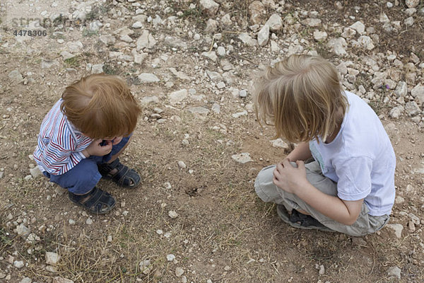 Zwei Jungen  die auf ein Loch im Dreck blicken.