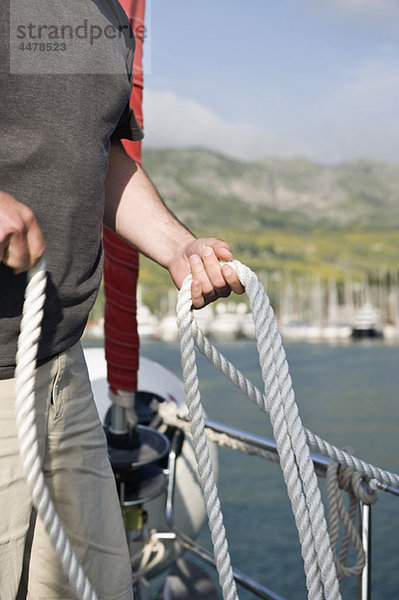 Mann auf einem Segelboot mit Halteseil