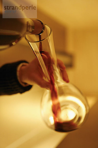 Detail einer Person  die Rotwein in eine Karaffe gießt