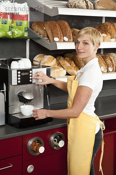 Eine Verkäuferin  die eine Espressomaschine in einem Bäckerei-Café benutzt.