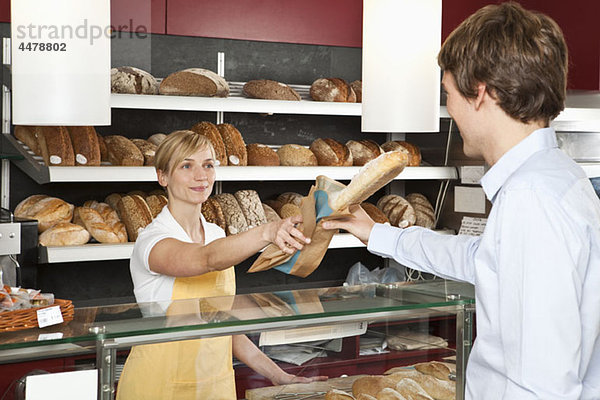 Ein Verkäufer  der einem Kunden in einer Bäckerei hilft.