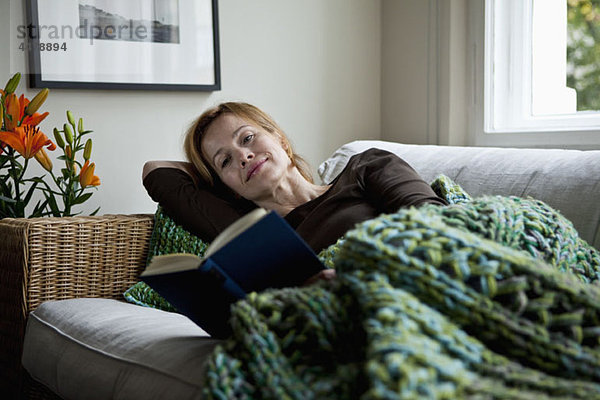 Eine Frau liest ein Buch  während sie auf dem Sofa liegt.