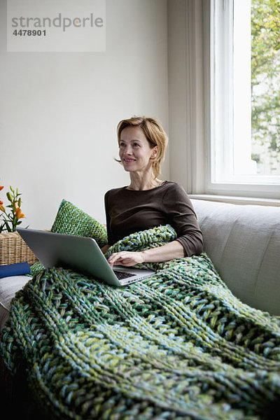 Eine Frau  die auf einer Couch liegt und einen Laptop benutzt.