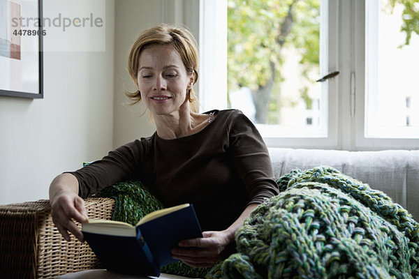 Eine Frau liest ein Buch  während sie auf dem Sofa liegt.