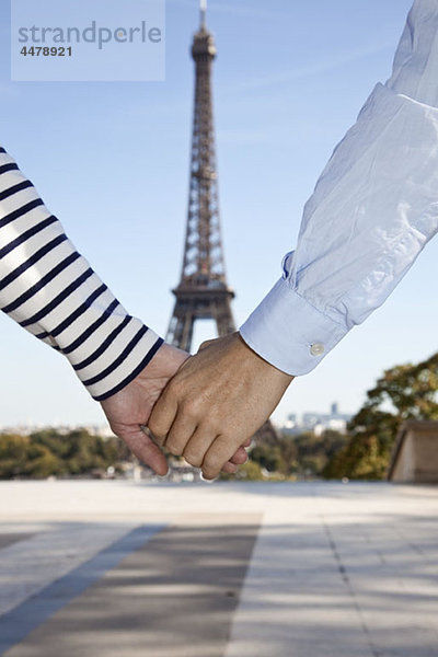 Ein Mann und eine Frau halten sich vor dem Eiffelturm an den Händen.