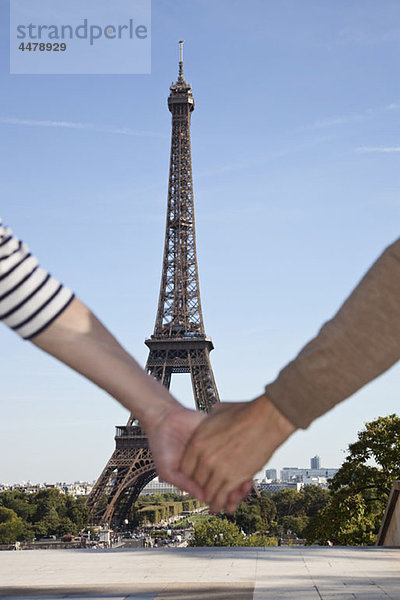 Ein Mann und eine Frau halten sich vor dem Eiffelturm an den Händen.