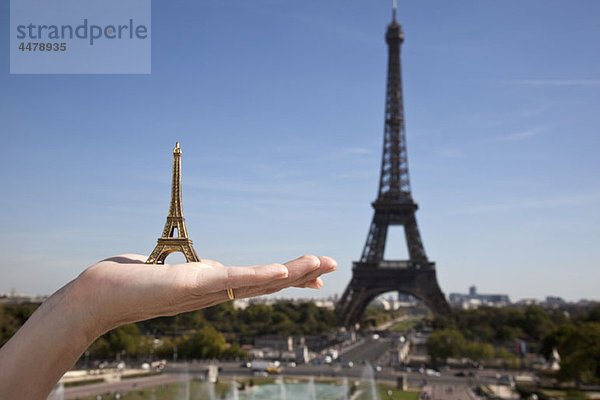 Eine Frau hält ein Eiffelturm-Souvenir neben dem echten Eiffelturm.