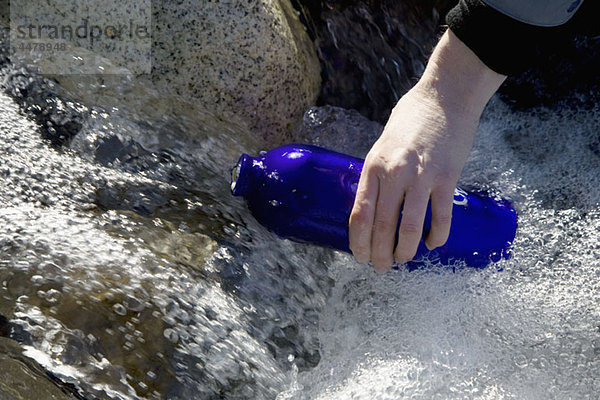 Detail einer Person  die eine Trinkflasche in einem Fluss füllt.