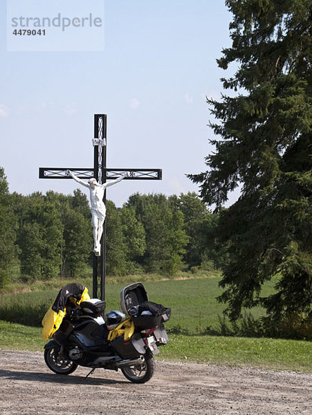 Ein Motorrad  das neben einem Kruzifix in einer ländlichen Gegend steht.