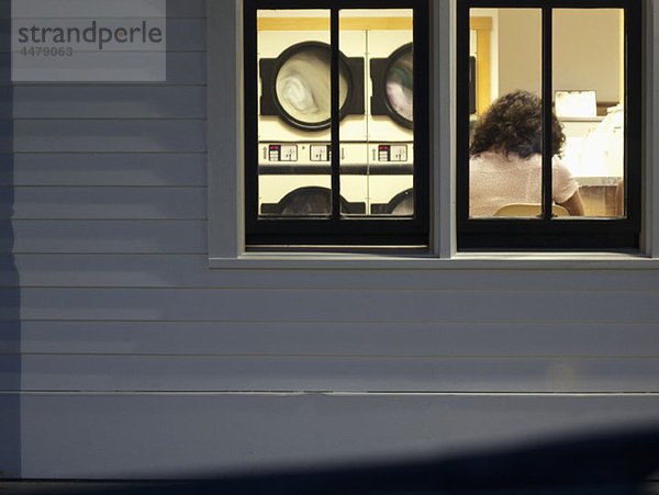 Eine Frau in einer Wäschematte  Rückansicht durchs Fenster